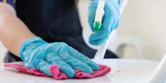 Manos con guantes limpiando la superficie de una mesa