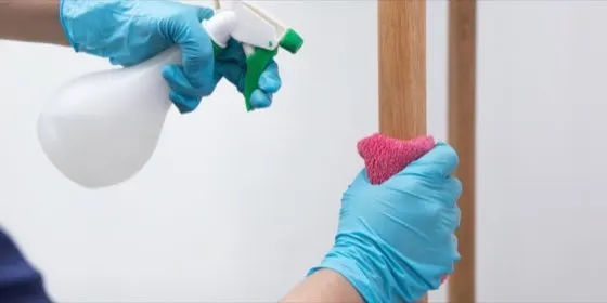 Manos con guantes aplicando producto sobre un mueble de madera